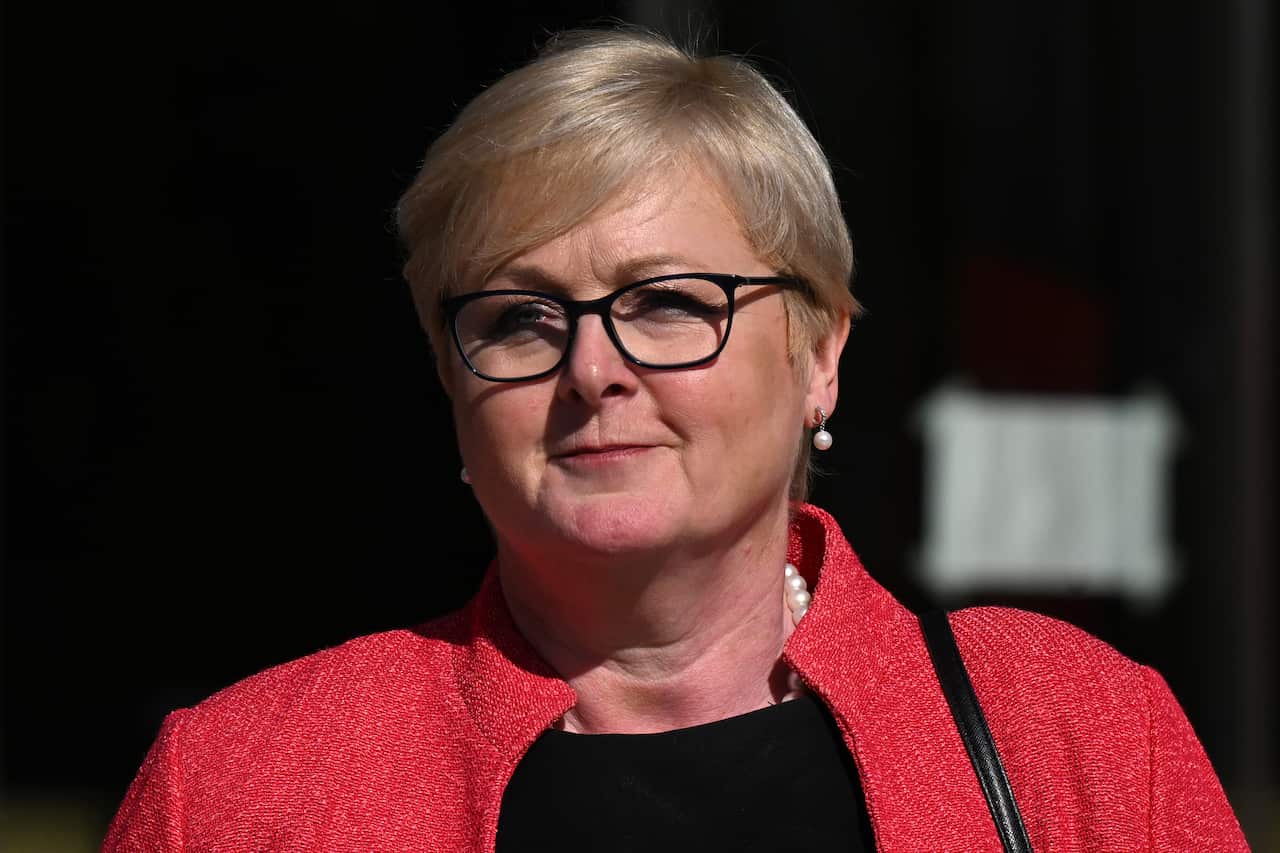 A woman wearing glasses, a black top, and a red blazer.