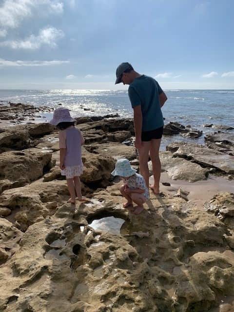 Two young girls and their father exploring rock pools by the ocean.