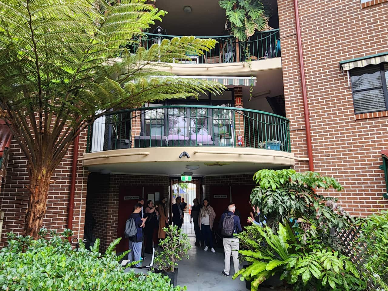 About 10 people gathered at the entry to a multi level apartment complex.