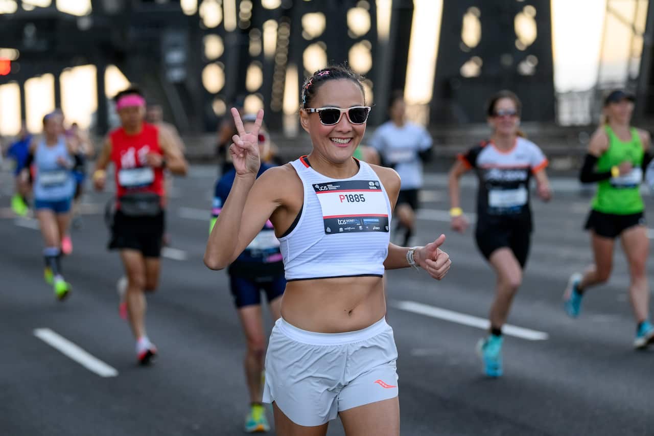 A woman shows the V sign as she runs a marathon with other runners around her.