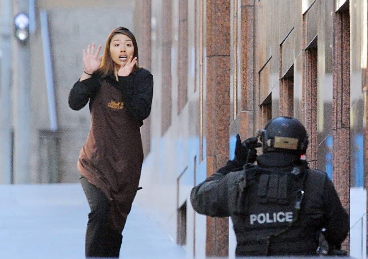A woman in a brown apron runs towards an officer wearing black tactical gear