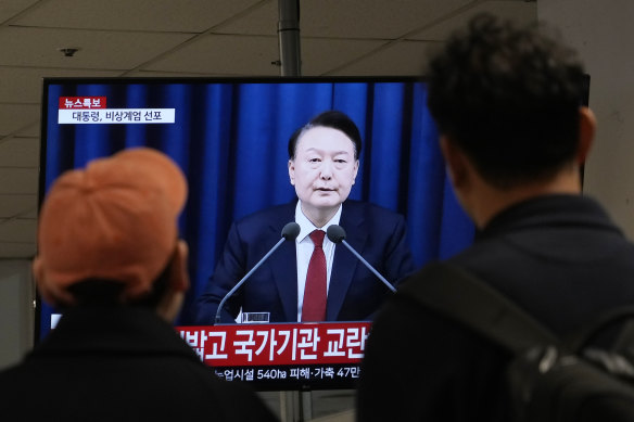 People watch a TV screen showing South Korean President Yoon Suk Yeol’s televised briefing.
