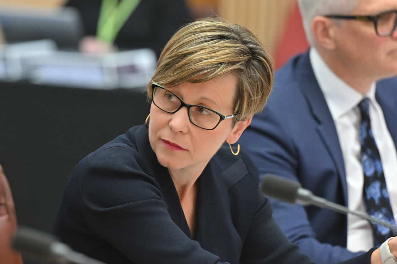 A woman with cropped hair and a blue blazer sits in front of a microphone 
