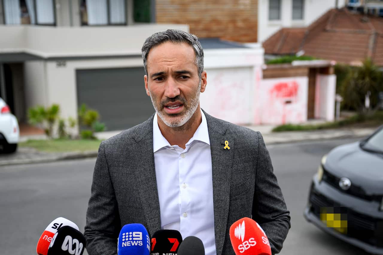 A man in a grey suit speaks to the media.