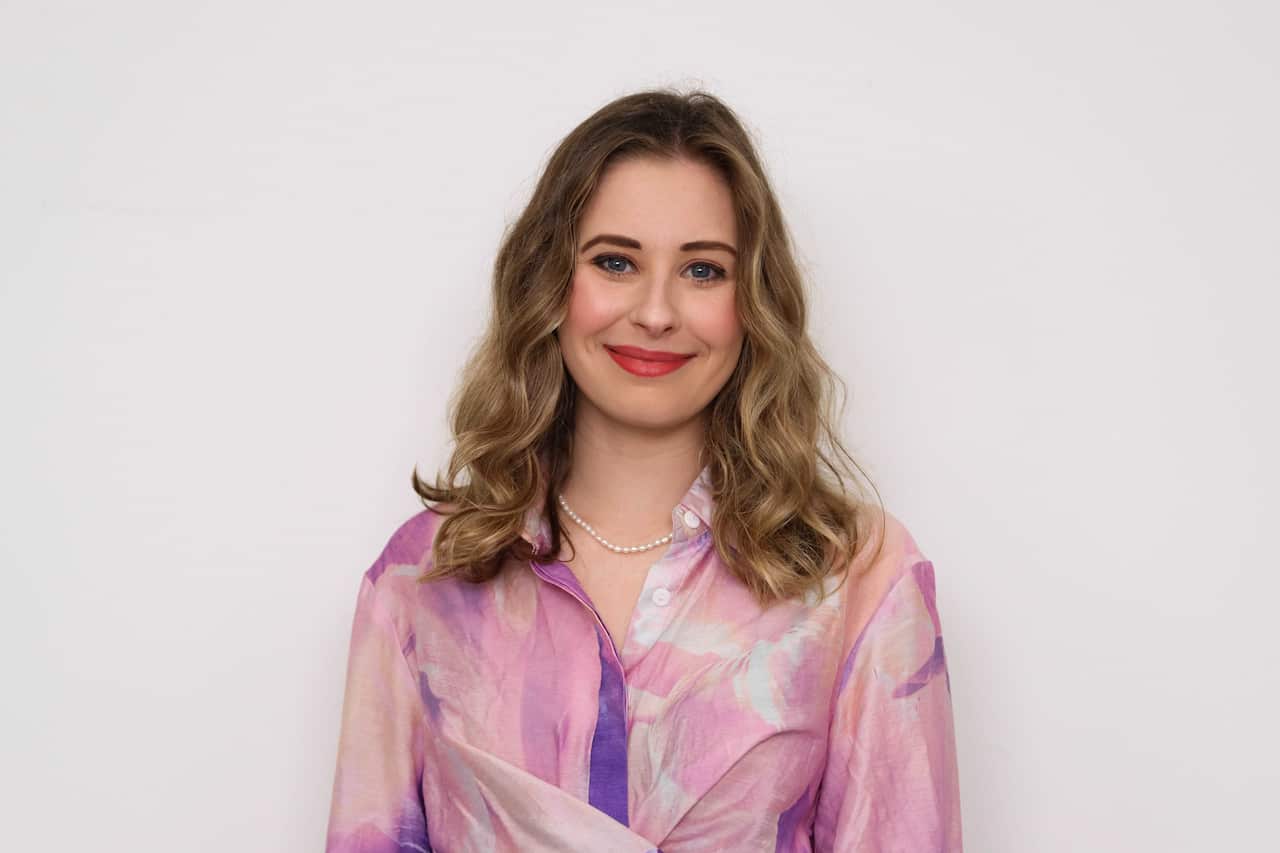 A woman in a pink blouse smiles.