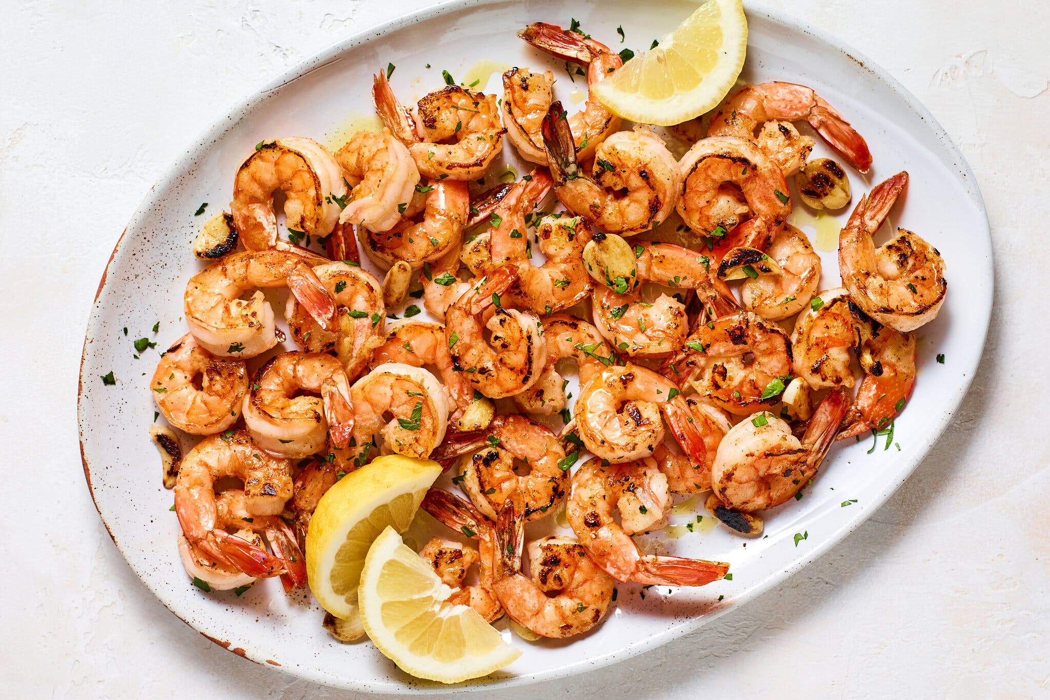 An overhead image of a white platter topped with shrimp and a few lemon wedges.
