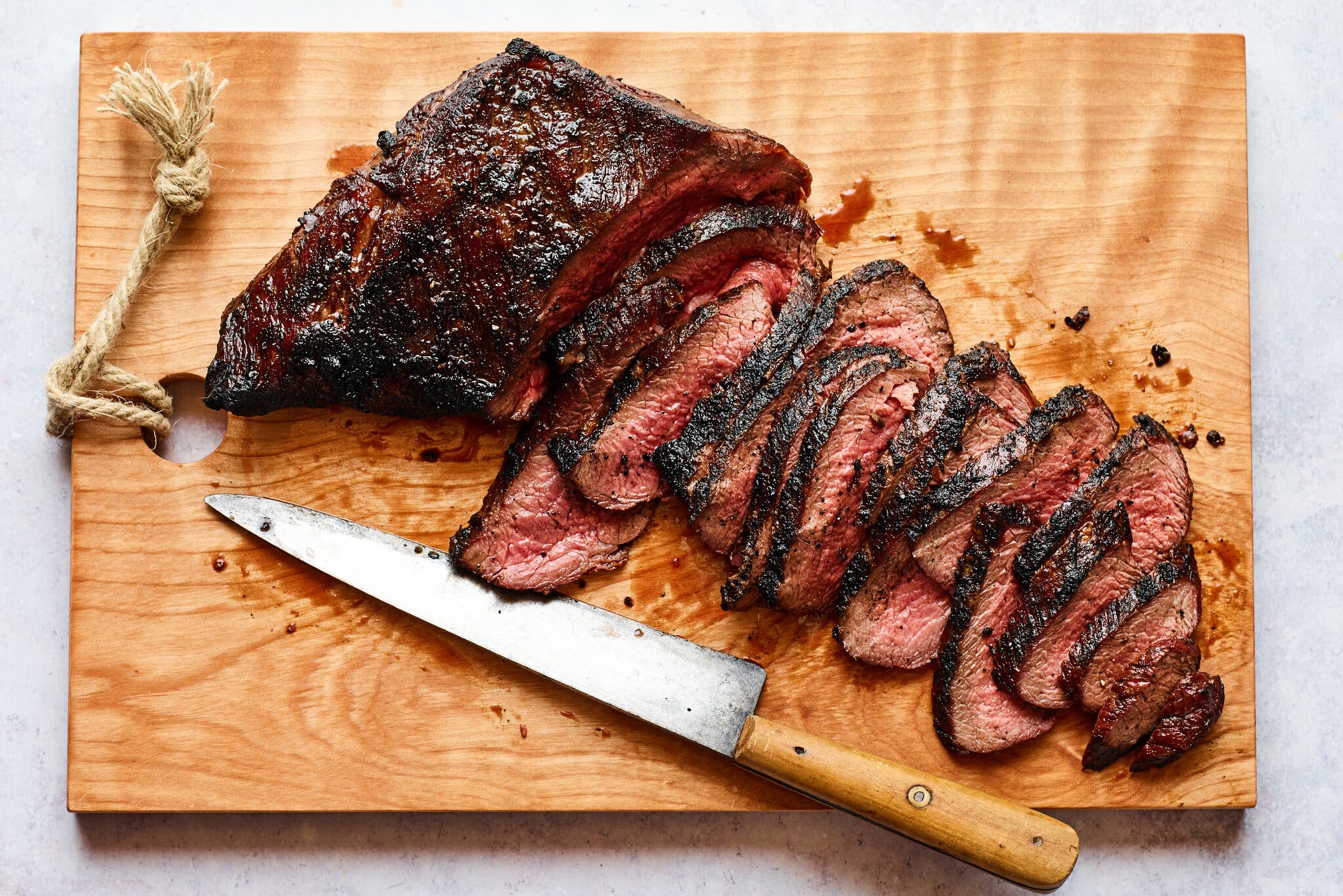 An overhead image of a grilled steak, sliced thinly on a cutting board. A knife sits just below.