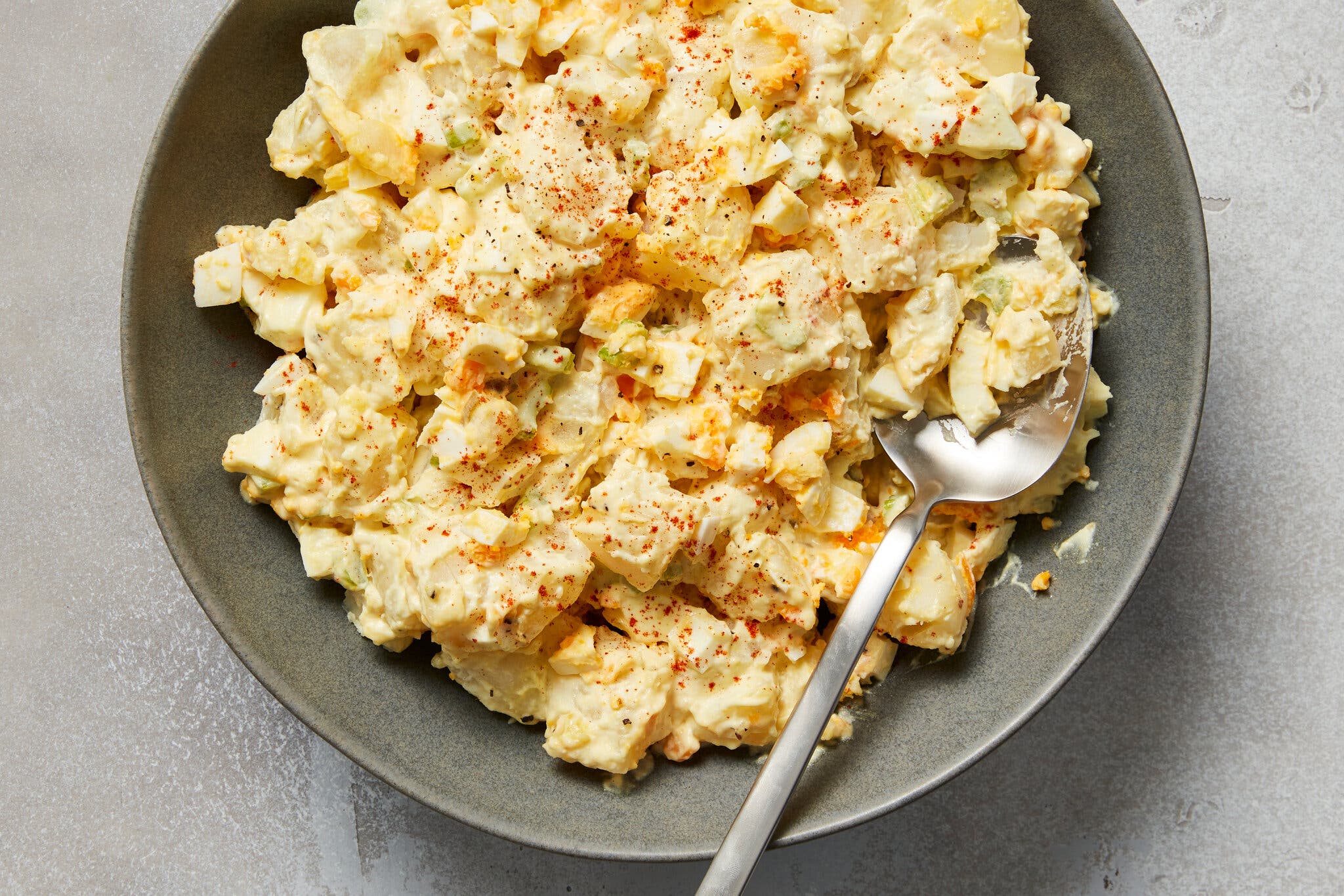 An overhead image of a gray bowl holding cubed potatoes coated in a mayonnaise-based sauce and sprinkled with paprika.