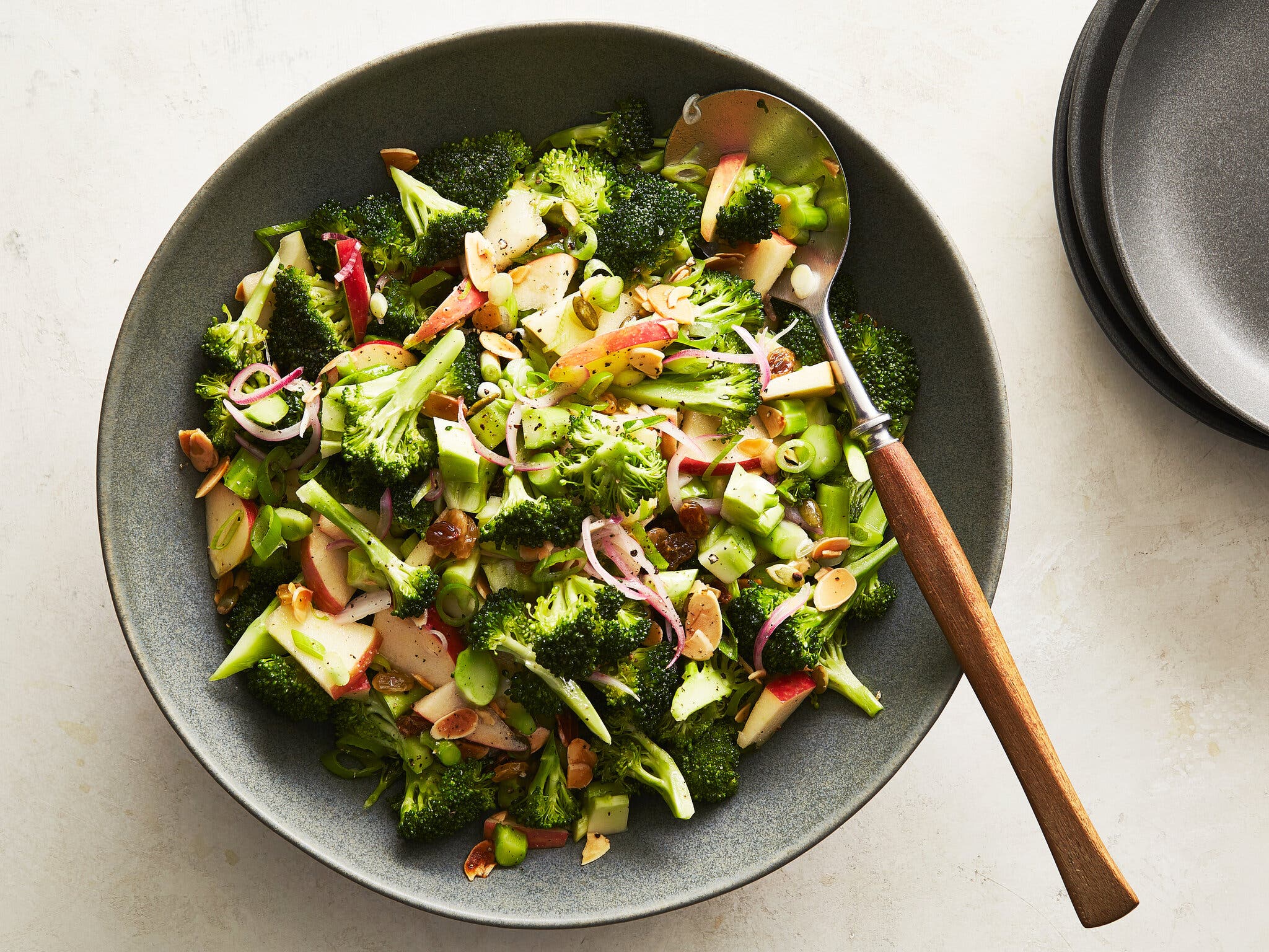 An overhead image of a gray bowl filled with pieces of broccoli, apple chunks and nuts.