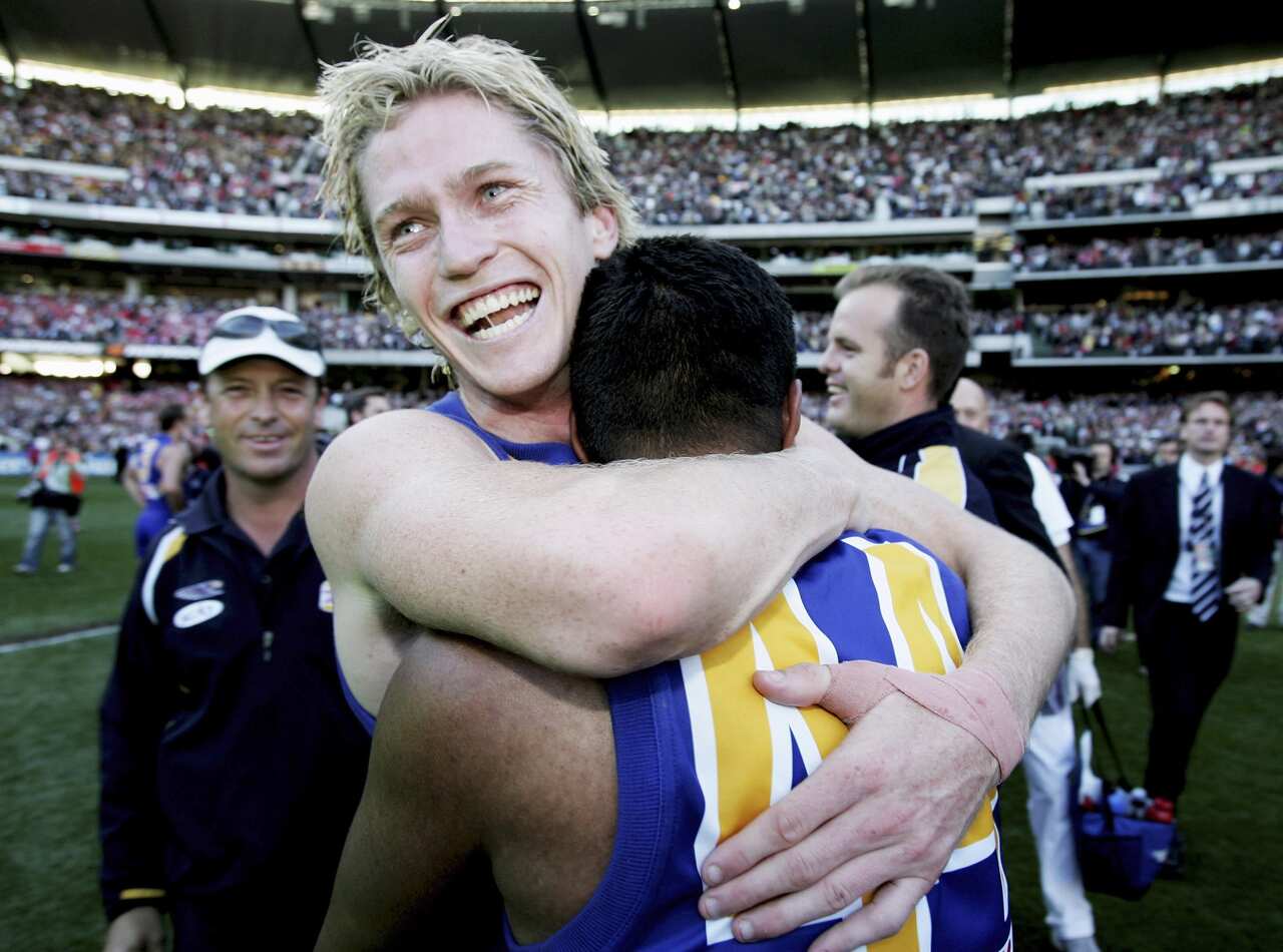 A man with blonde hair in a football uniform smiling and hugging another player on the field.