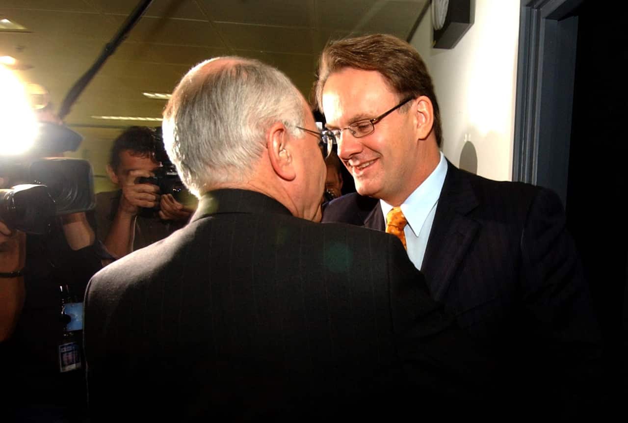 Two men lean in close as they firmly shake each others hands.