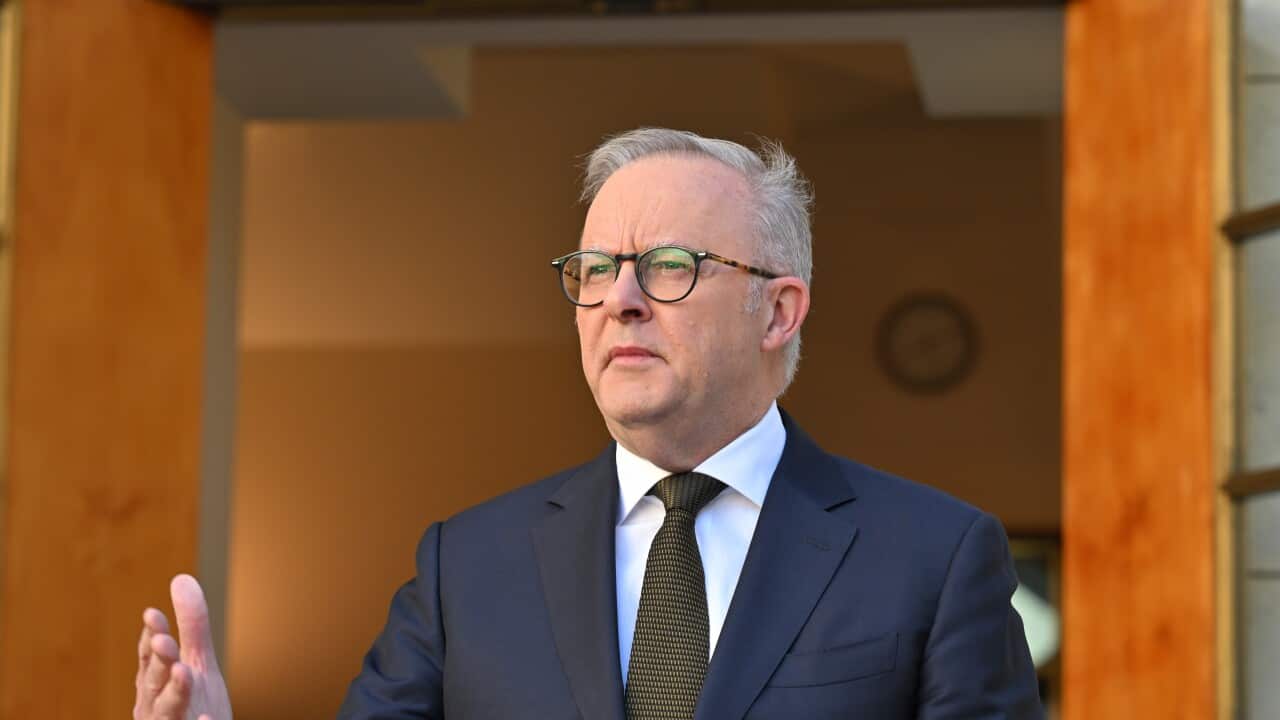 A middle aged white man wearing a dark suit and glasses. He has his right hand in front of him.