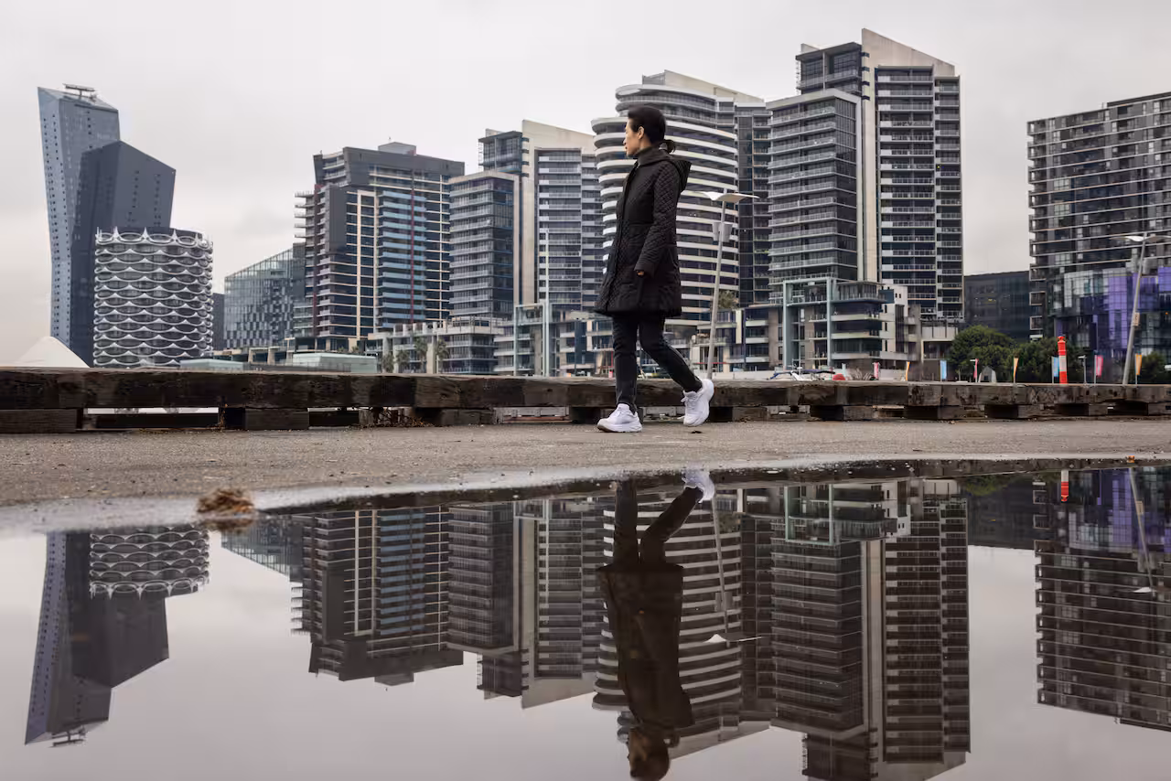 A woman in black winter clothes walks past the Melbourne sky line on a cold morning.