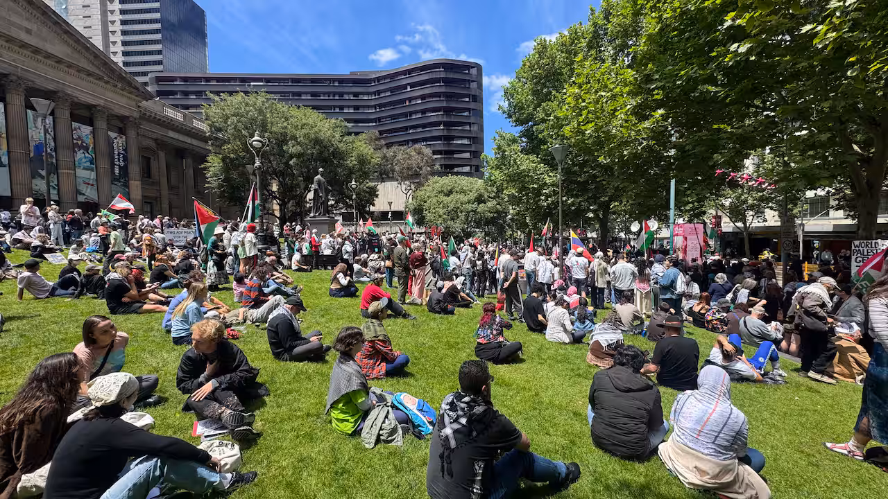 Protesters gather on the grass in a park.