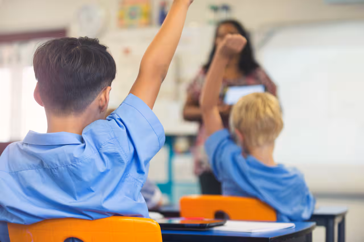 Two students in a classroom putting up their hand.