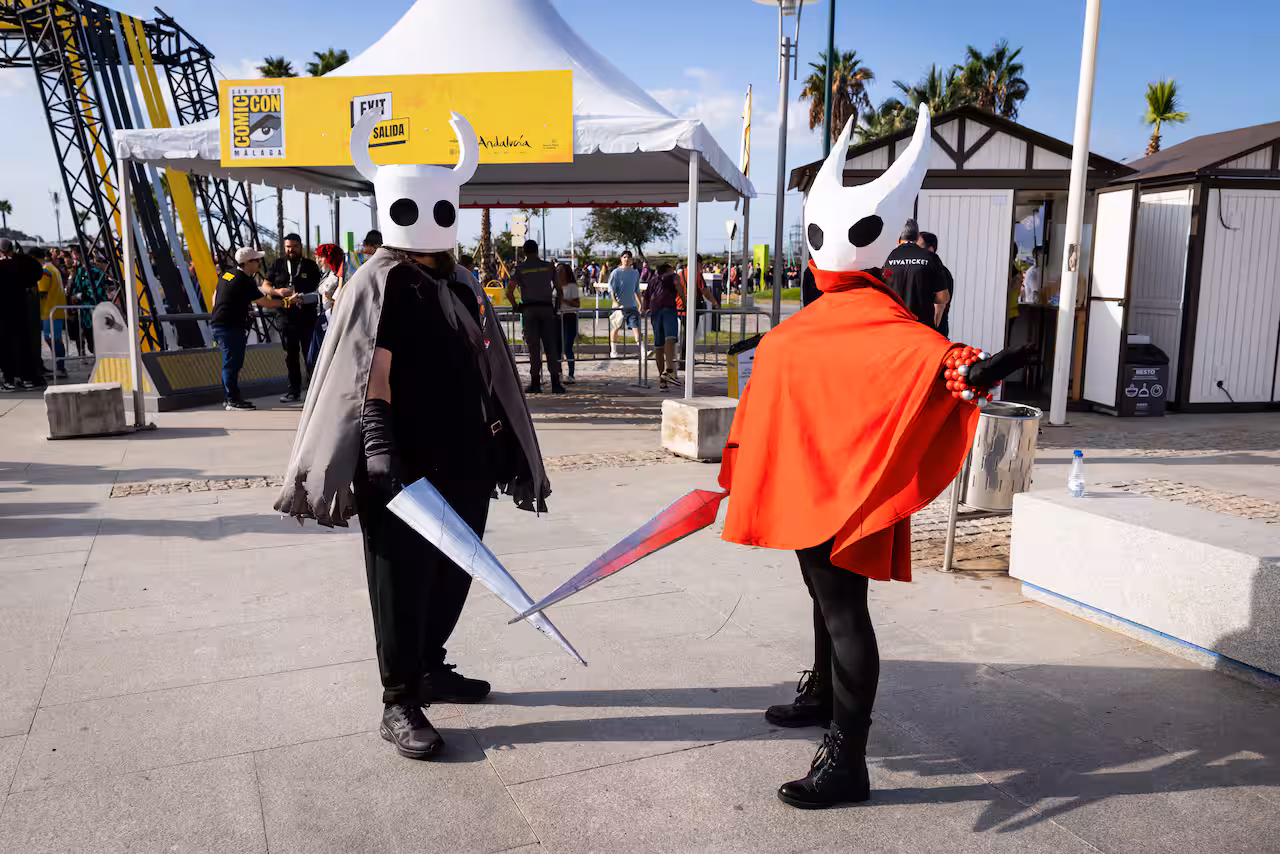 Two people dressed up as characters from the game Hollow Knight, with swords and large insect heads.