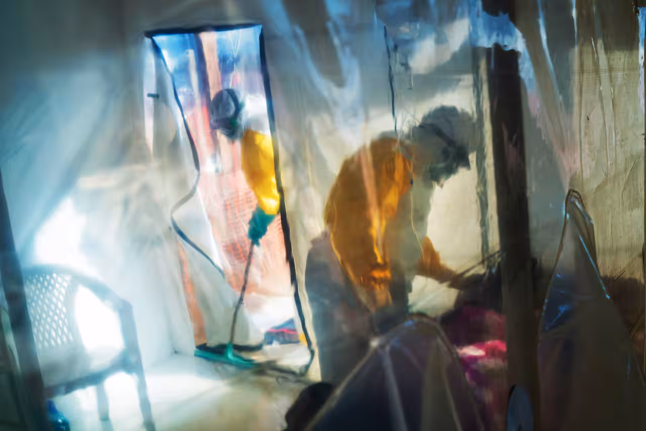 Health workers wearing protective suits tend to to a patient kept in an isolation tent.