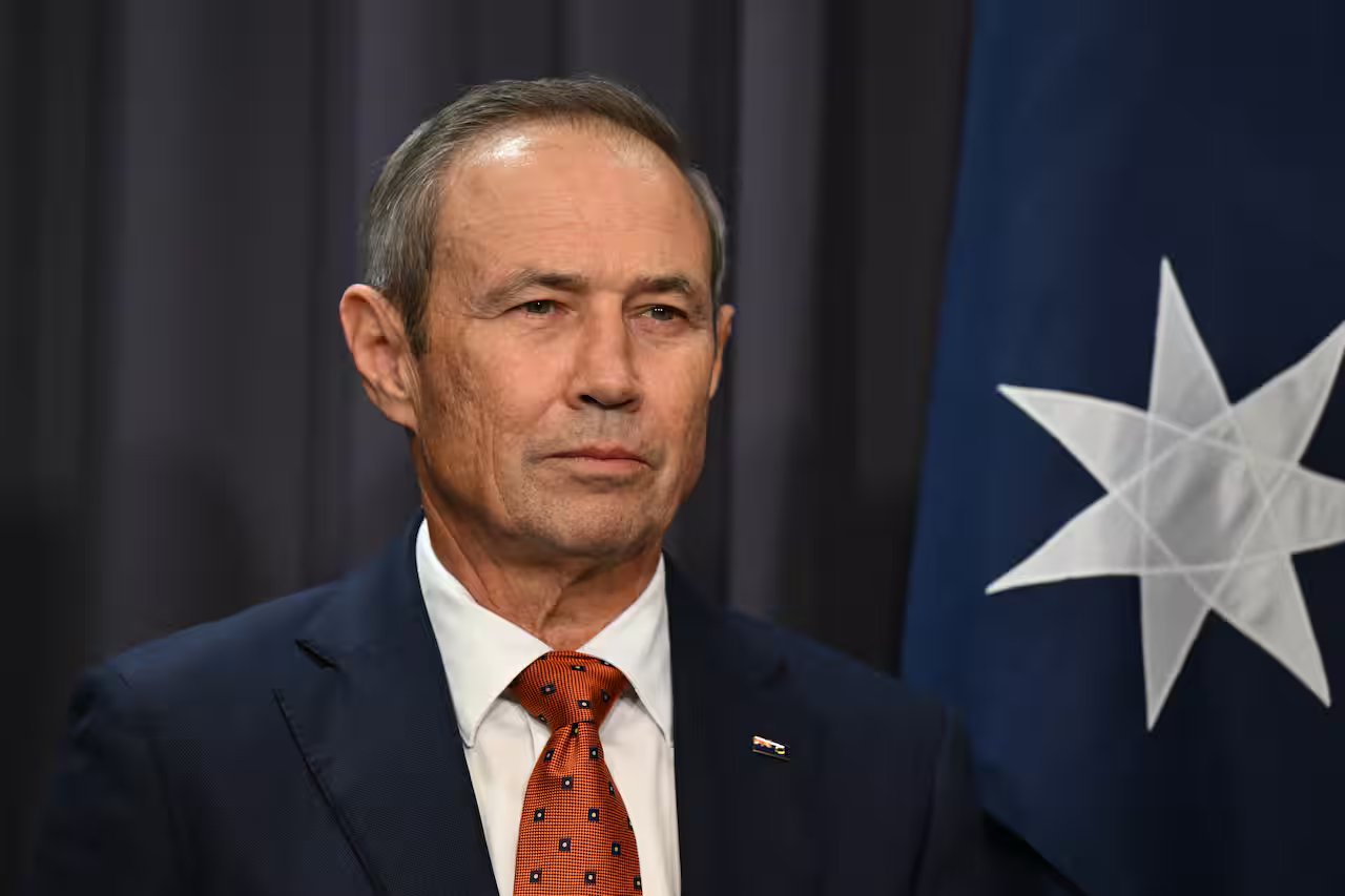 A middle-aged white man wearing a navy suit, white shirt and red tie. 