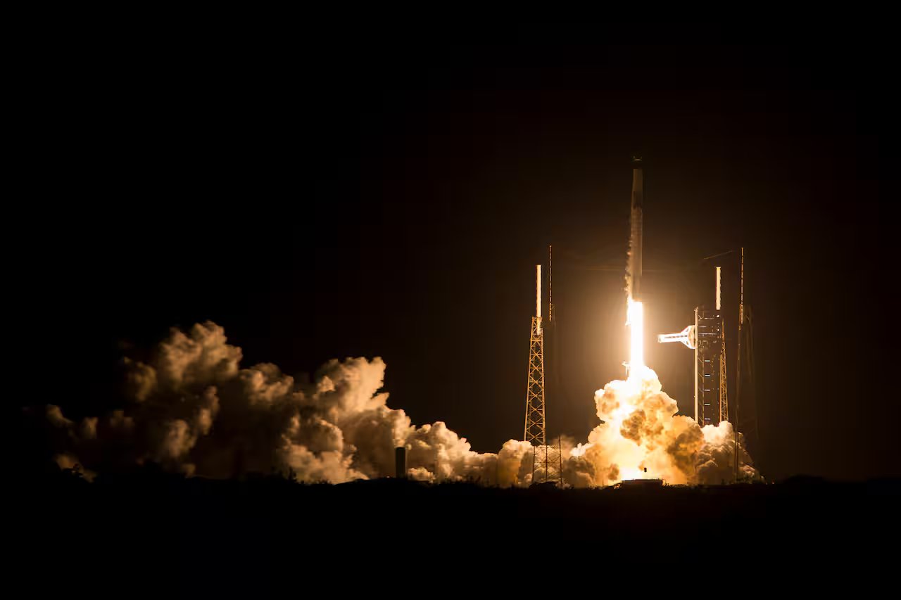 A rocket launches towards the sky with fire and a plume and smoke below.