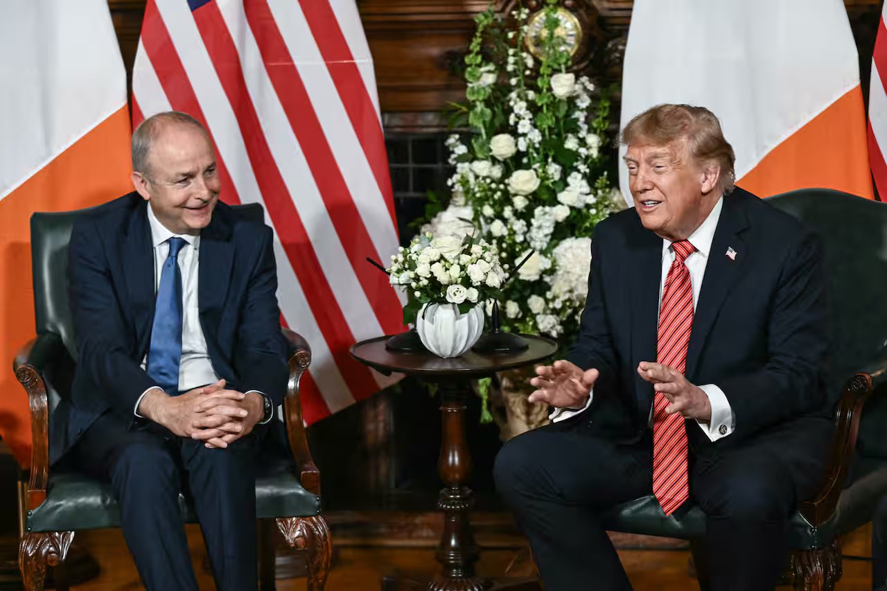 US President Donald Trump gestures while speaking during a seated meeting with Irish Prime Minister Micheál Martin, with American and Irish flags in the background.