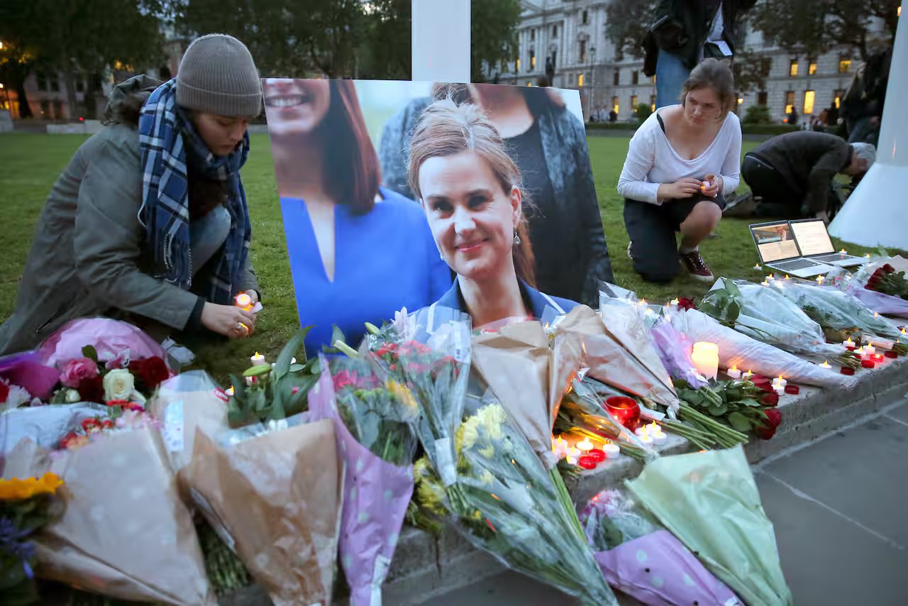 Two women add candles to a collection of flowers and candle surrounding a picture of UK MP Jo Cox