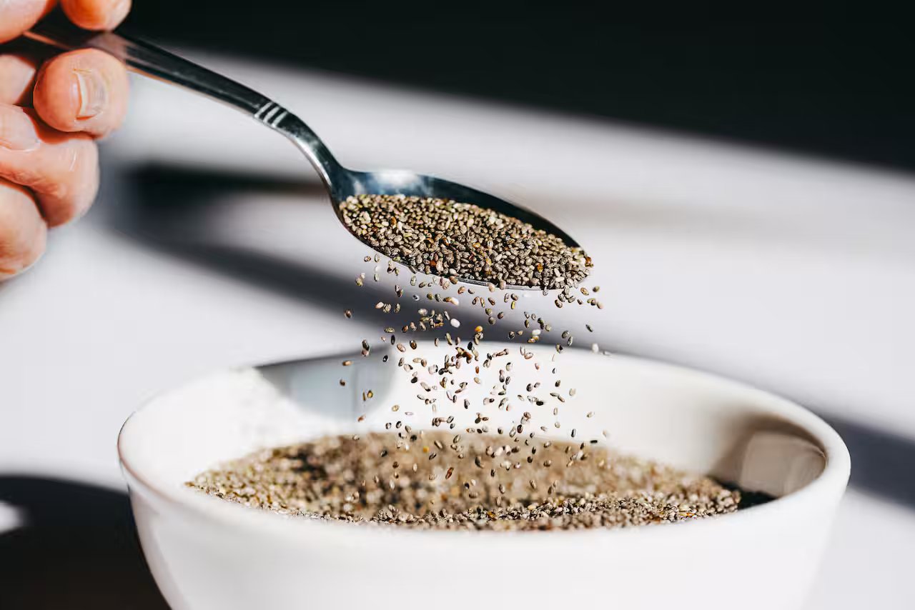 Light shines on a spoon as chia seeds are poured into a white bowl, creating a dynamic motion