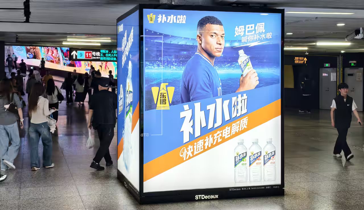 Pedestrians pass by an electrolyte drink advertisement for French football player Kylian Mbappé in the subway in Shanghai