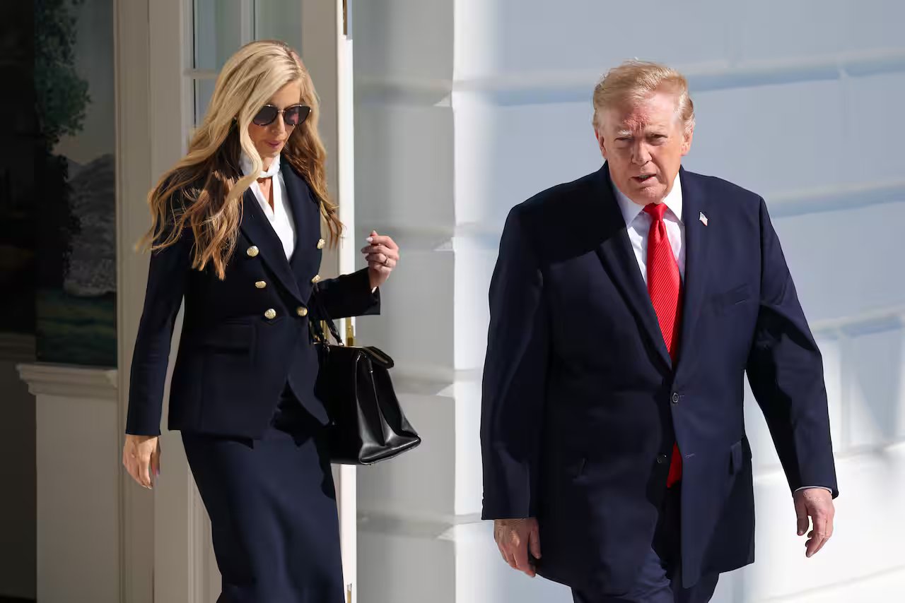 A woman walking behind a man, both wearing dark suits.